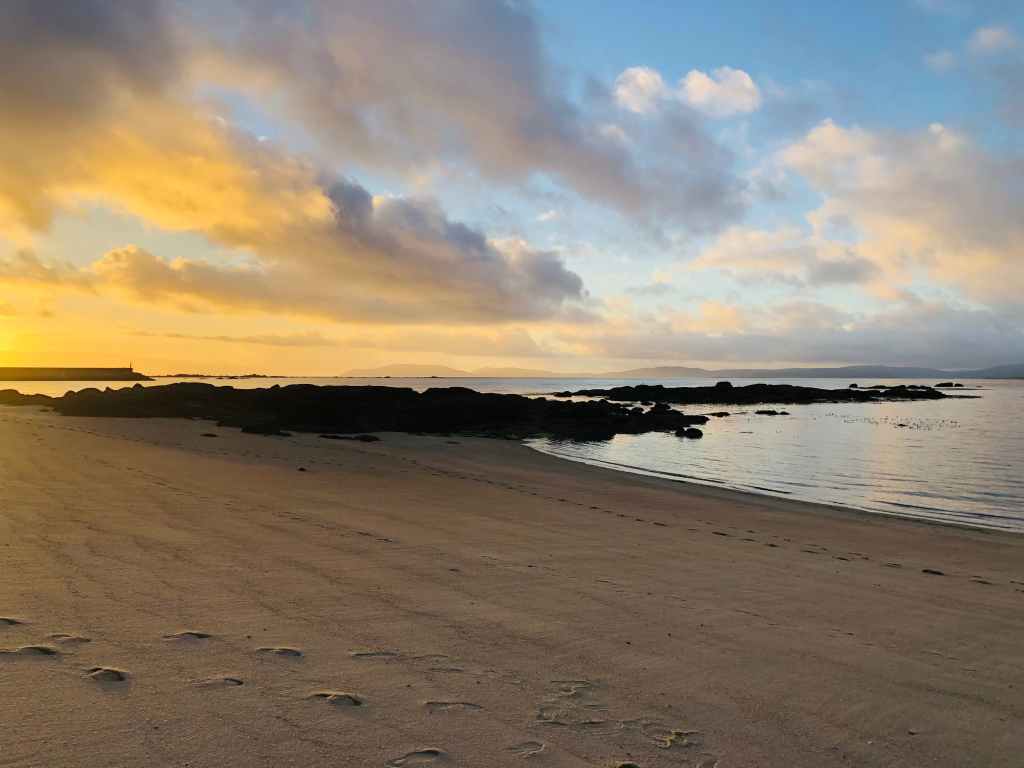 Praia deserta ao solpor con marea baixa, ceo anubrado e pegadas na area.